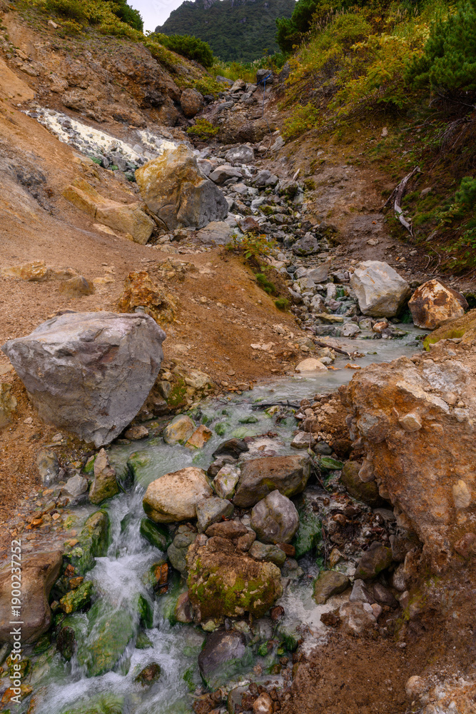 Obraz premium A serene stream winds through rugged rocks and earth, showcasing nature's beauty in Russia's landscape. Clear water gently flows, creating a soothing atmosphere amidst the wilderness.