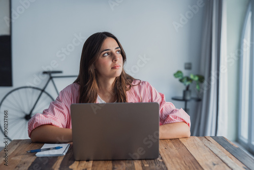 Quadro em tela A frustrated and stressed woman sits at her desk near a laptop, holding her head