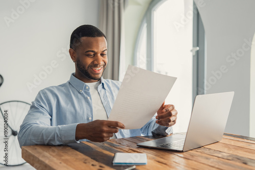Schilderij op canvas Happy smiling cheerful African American man reading letter at workplace, sitting