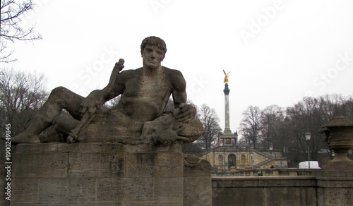 Obraz na plátně Allegorical statue symbolizing a Bavarian tribe on an Isar River bridge, with the Friedensengel monument rising in the background, Munich, Germany, DE, 17 Feb