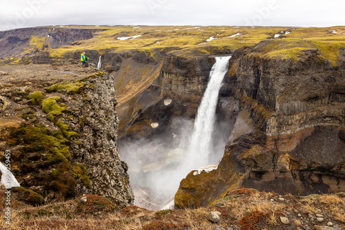 Haifoss waterfall in Fossardalur valley with a traveler sitting on a cliff edge Iceland