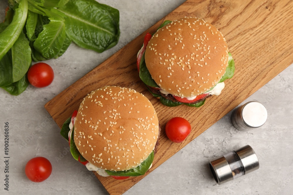 Naklejka premium Delicious burgers with meat patties on grey table, flat lay