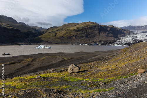 Solheimajokull glacier lagoon with volcanic ash striped iceberg and mossy moraines, Iceland