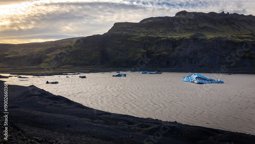 Solheimajokull glacier lagoon with floating blue icebergs and volcanic ash moraines at sunset, Iceland