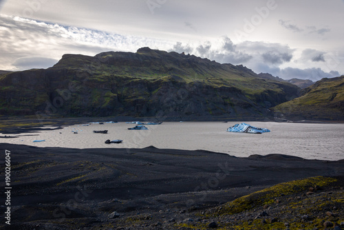 Solheimajokull glacier lagoon with floating blue icebergs and volcanic ash moraines, Iceland