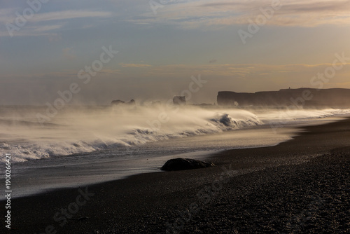 Dangerous sneaker waves crashing on Reynisfjara Black Sand Beach at sunset with Dyrholaey in the distance, Iceland
