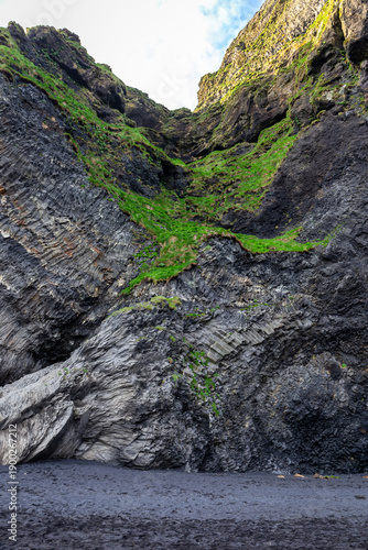 Bent basalt columns and mossy cliffs at Halsanefshellir Cave on Reynisfjara Black Sand Beach, Iceland