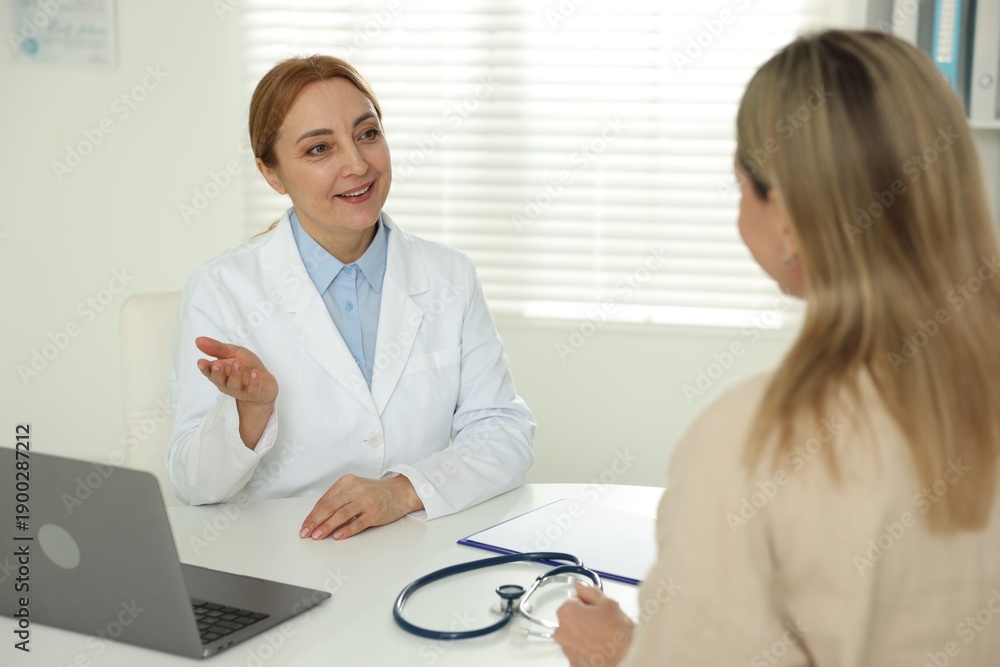 Obraz premium Woman having appointment with smiling cardiologist at table in clinic, selective focus