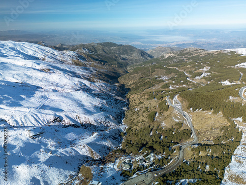 Drone view of Sierra Nevada Spain with winding mountain road, snow covered slopes and distant valley, ideal background for travel, nature, adventure and winter tourism concepts.