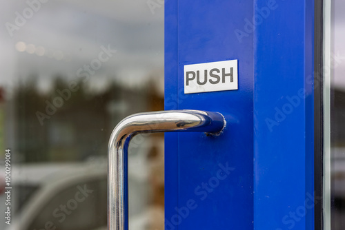 Fotografie Close-up of metal door handle with push sign on blue frame and glass door