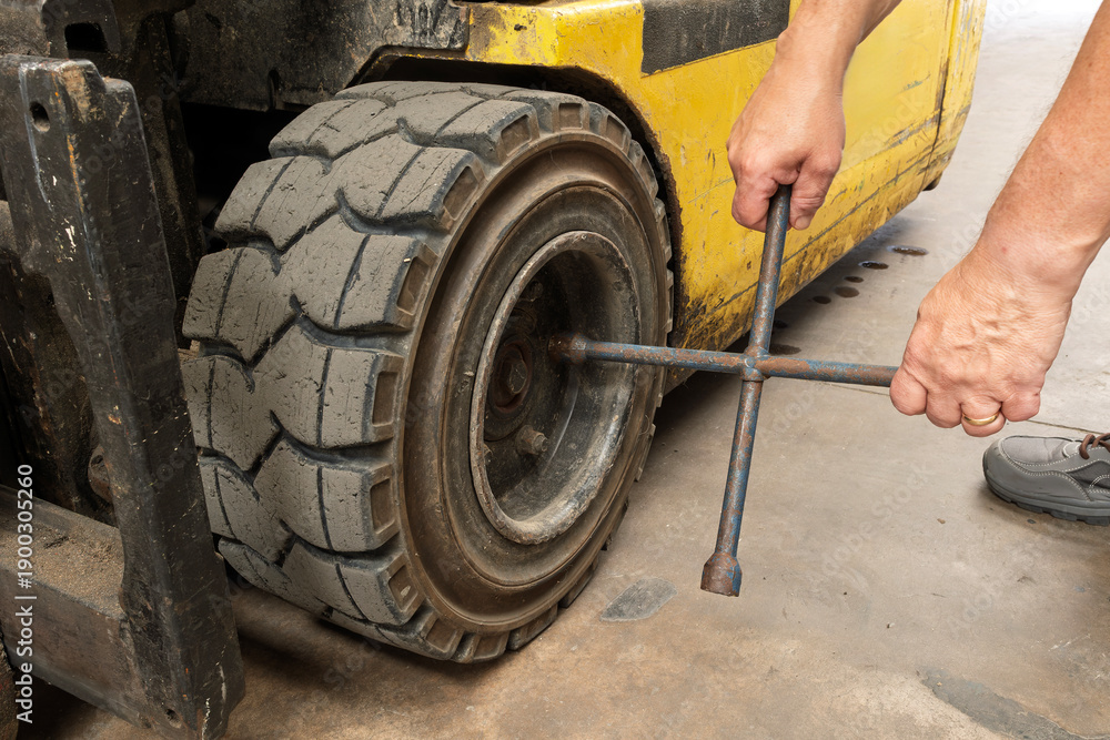 Fototapeta premium Warehouse Worker Changing Forklift Tyre Using Wrench
