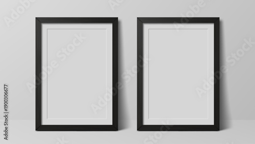 Two empty vertical photo frames in black stand on white wall. Realistic graphic design element for mockup template or product display.