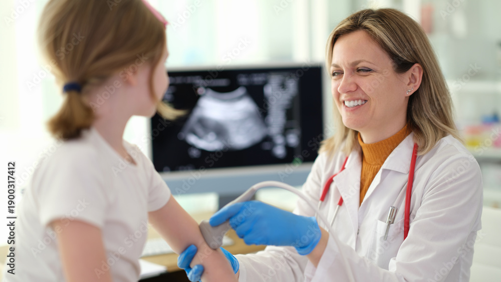 Obraz premium A kind doctor smiles warmly as she examines a young girl's arm with a medical device in a well-lit clinic. The atmosphere is friendly and reassuring, promoting health and care.