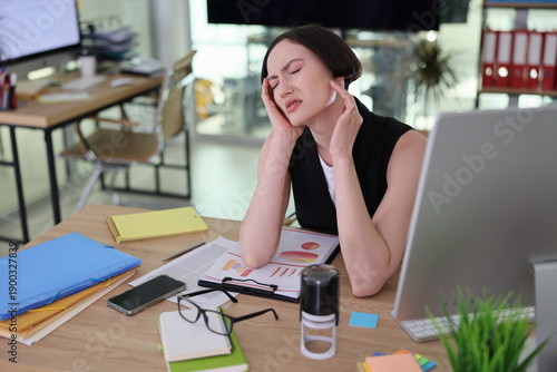 Tableau sur toile In a vibrant office filled with natural light, a young woman rests her head in her hands, overwhelmed by tasks