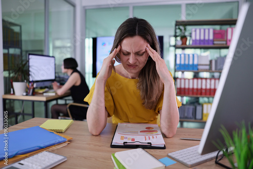 Tableau sur toile A woman sits at her desk with furrowed brows, trying to concentrate on her work while feeling stressed