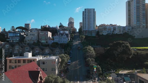 Wide aerial shot following a cable car climbing the steep incline of Hyde Street on a crystal clear day in San Francisco, California. 4K