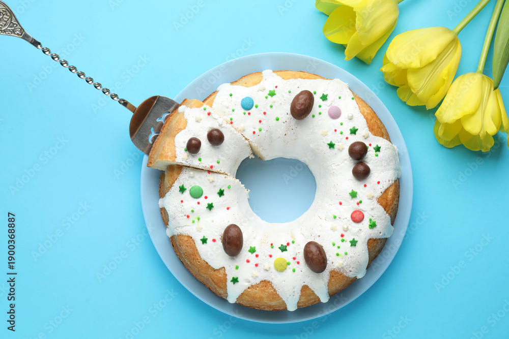 Fototapeta premium Delicious Easter cake and yellow tulips on light blue background, flat lay