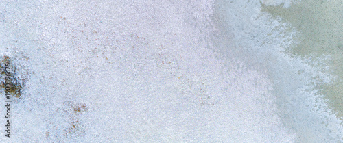 Detailed aerial texture of a winter landscape with light grey mud and white frost creating a soft and complex natural background from above