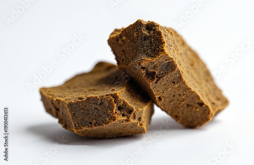 Two chunks of brown hashish resin are close up on a white backdrop. This cannabis concentrate is earthy textured and porous. Medical marijuana product.