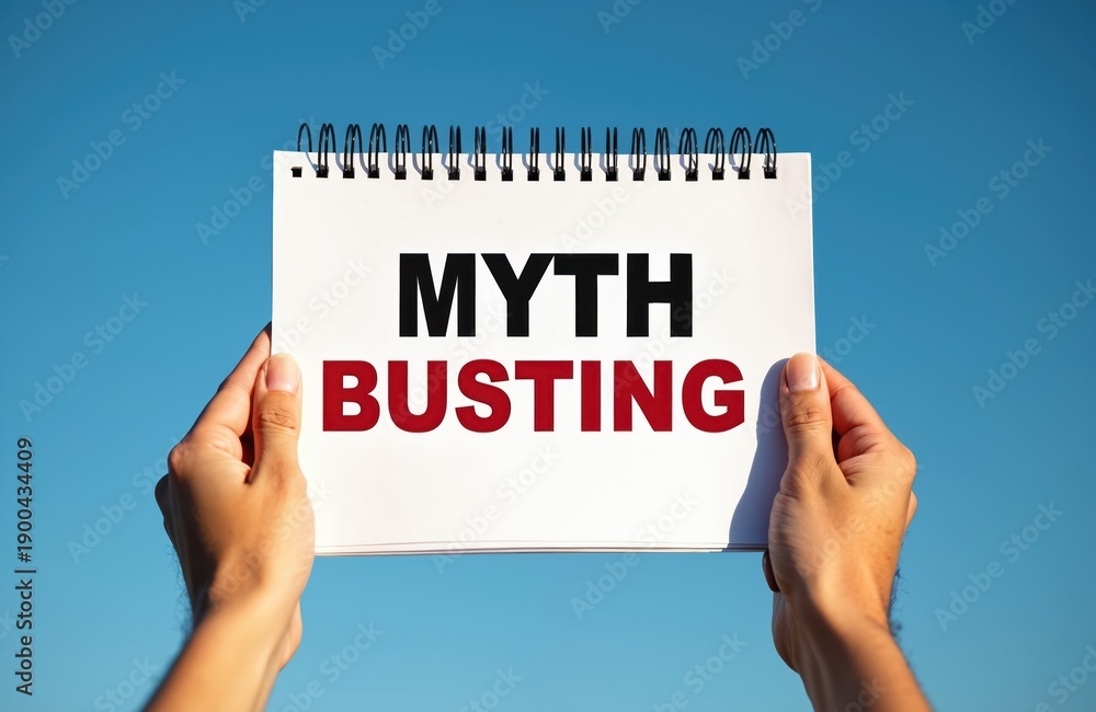 Fototapeta premium Hands hold notebook paper with MYTH BUSTING text against clear blue sky. Concept of challenging common beliefs, revealing truths, clarifying misconceptions with clear communication. Useful for