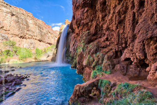 Canvas Print A waterfall is flowing into a river, with a lush green area surrounding it
