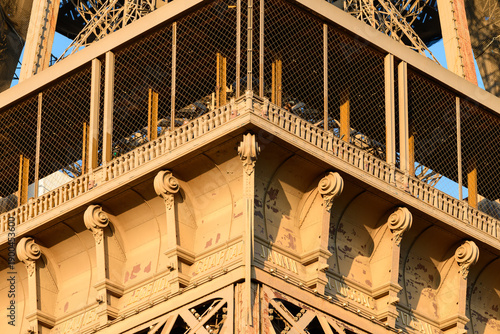 фотографія Close-up of the Eiffel Tower's ornate platform corner, bathed in warm golden sunlight, highlighting detailed ironwork, decorative corbels, and textured surfaces