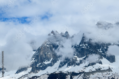 Konstfotografi Sharp rocky summits of Aiguille de Blaitiere emerge through drifting clouds, with patches of lingering snow and dramatic textures in the French Alps