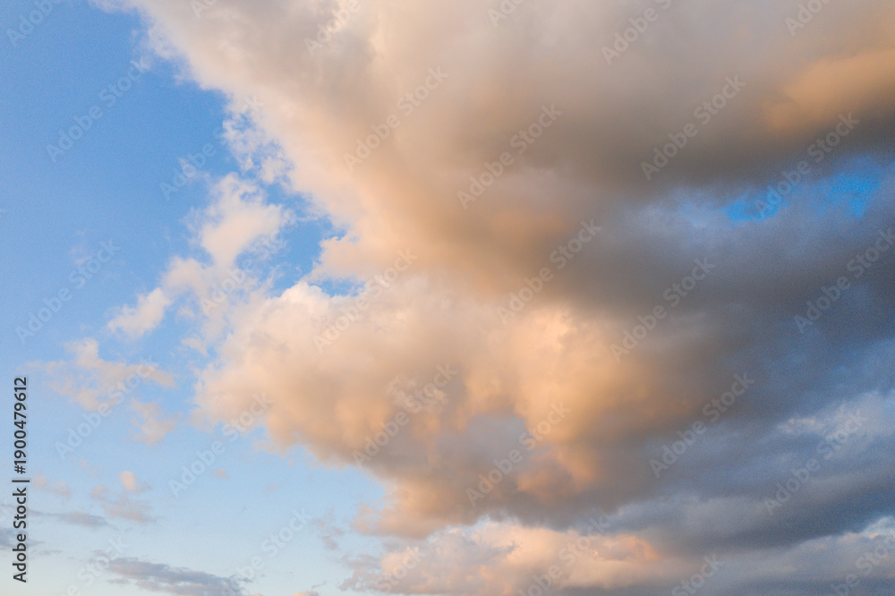 Obraz premium Gentle pastel-toned clouds float across a serene blue sky, illuminated by warm evening light and creating a peaceful, airy atmosphere.