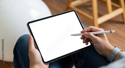 Person holds tablet with stylus for drawing or writing in a casual setting with wooden floor and