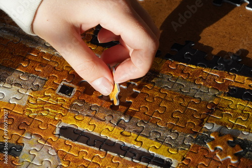 Fotografie A young person's hand connects a jigsaw puzzle piece into the jigsaw
