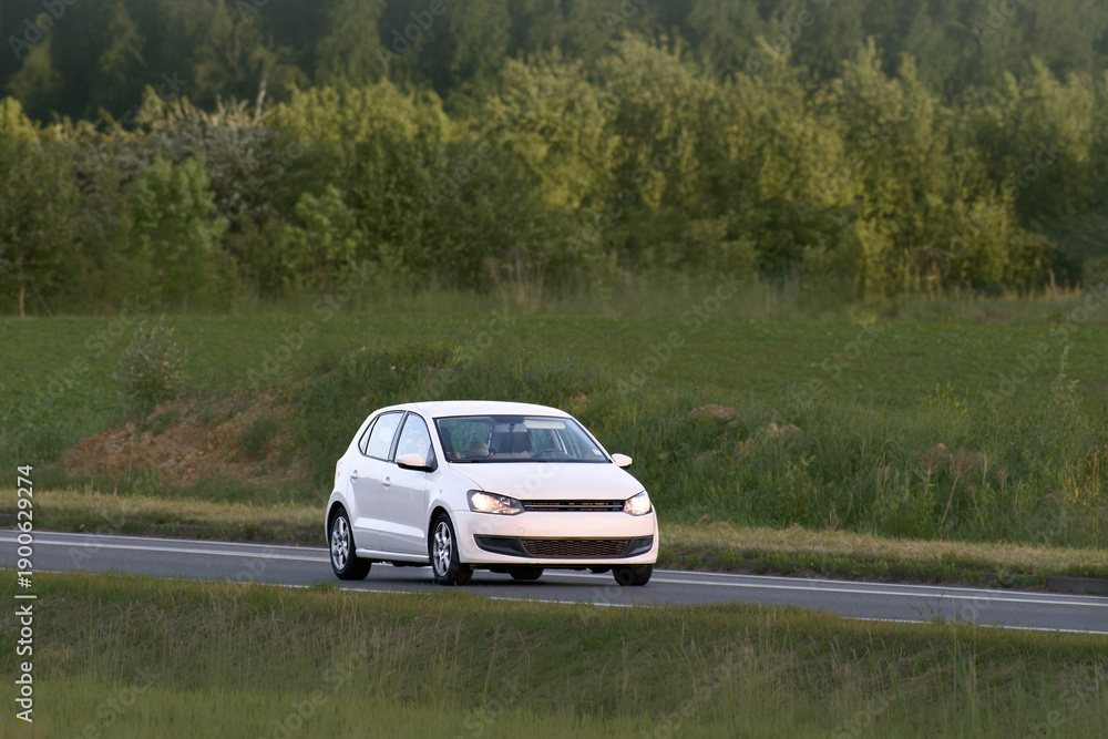 Fototapeta premium Urban hatchback driving through open green fields