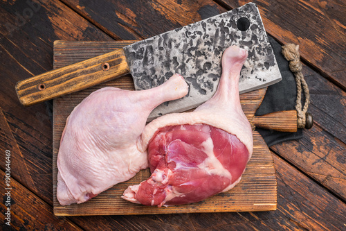 Fotografia Uncooked duck legs ready for cooking, set on a weathered wooden surface, with a cleaver and rosemary — warm, rustic tones