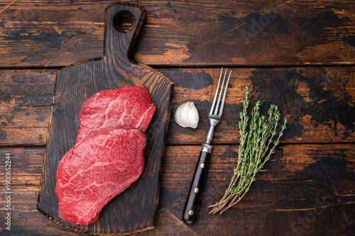 Fotografie Uncooked Wagyu chuck steak with deep texture placed on rustic board with herbs and garlic over weathered timber surface perfect for butcher content
