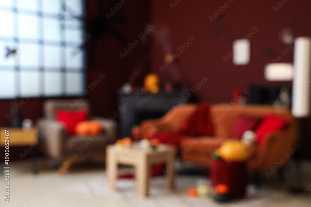 Fototapeta premium Blurred view of living room decorated for Halloween with sofa, armchair and fireplace