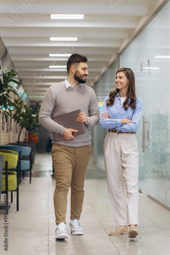 Business colleagues walking and conversing in modern office corridor, discussing work and networking