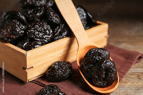 Dried prunes in wooden spoon and bamboo box on rustic table, close up of dehydrated plums, healthy organic snack, natural dried fruit ingredient