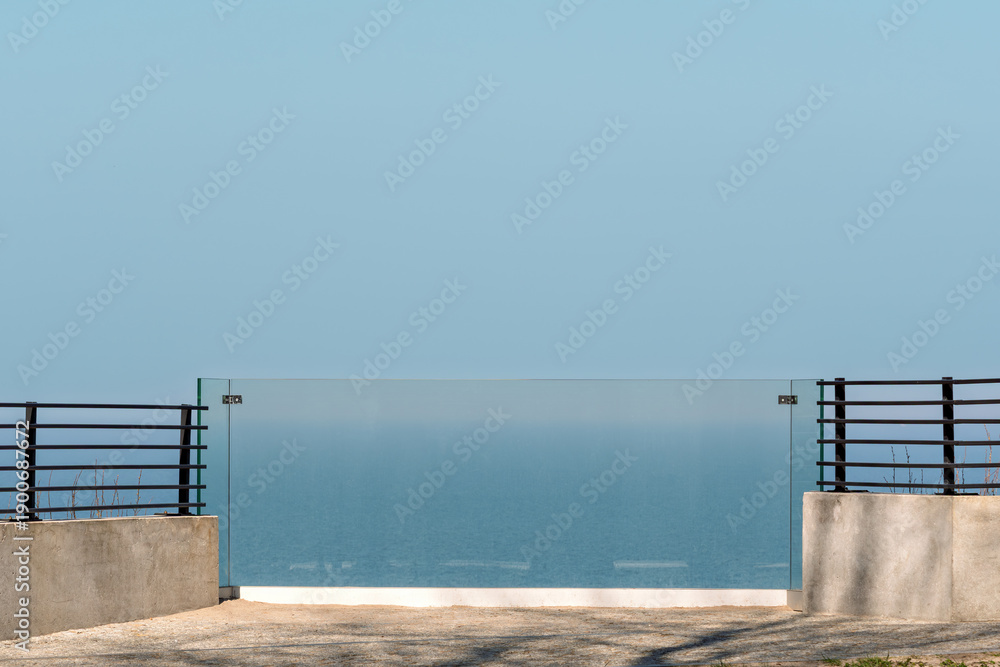 Obraz premium Minimal seaside terrace with glass railing and wide blue sky, calm backdrop for luxury real estate, travel escape, or wellness ads.