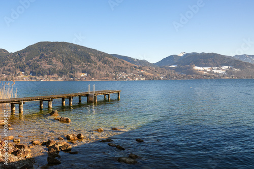 Wallpaper Mural Picturesque view of Lake Tegernsee in Bavaria, Germany. Typical atmosphere of the region with clear water, a wooden bathing jetty, reeds growing on the shore, and striking mountain silhouettes. Torontodigital.ca