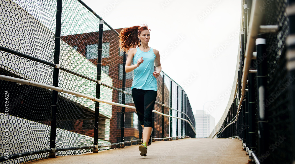 Fototapeta premium Fitness, running and woman in city for practice, wellness and challenge for health benefits. Outdoor, person or runner with exercise, morning jog or training with cardio, low angle or intense workout