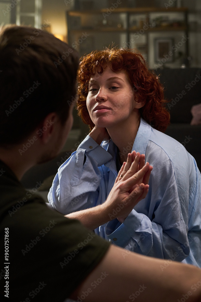 Fototapeta premium Vertical shot of Caucasian young adult woman smiling and touching hands with Caucasian young adult man indoors, both sitting close together and engaging in intimate interaction