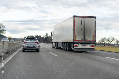 Silver SUV driving behind large semi-trailer truck on a multi-lane highway on an overcast day