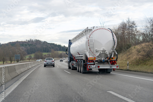 White tanker truck travels down a busy highway under an overcast sky during daylight hours
