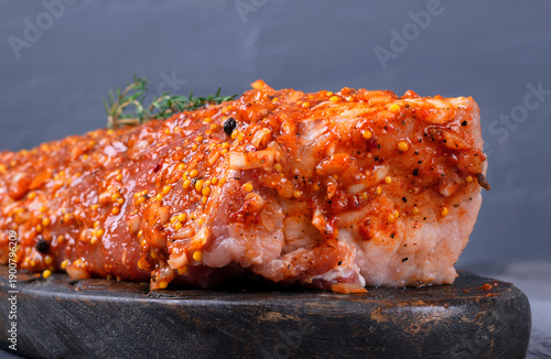 Pork neck meat covered with onion marinade with of grainy mustard, oil, spices and herbs on a gray background. Preparing meat for cooking. Side view, close-up