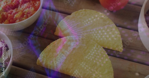 Showing two yellow tacos on wooden slats, bowls with salsa, salad, pale dip and purple reflections