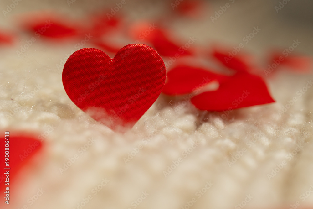 Fototapeta premium Red fabric hearts are scattered across a soft, textured surface, creating a romantic atmosphere perfect for Valentine's Day inspired digital content.