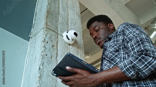 Worker inspects security camera on wall in modern office setting during daylight hours