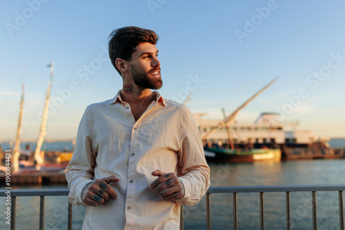Handsome man at the Lisbon harbor wearing a light shirt, enjoying sunset by the water