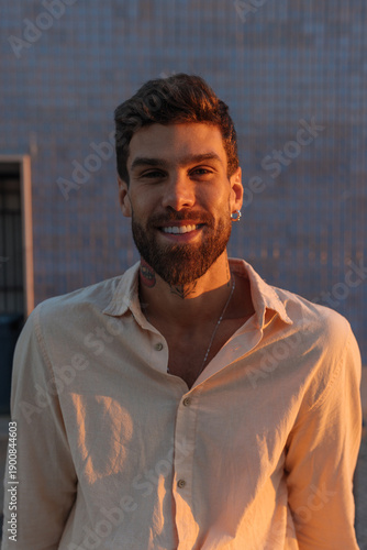 Smiling man with beard in beige shirt outdoors during golden hour sunset warmth
