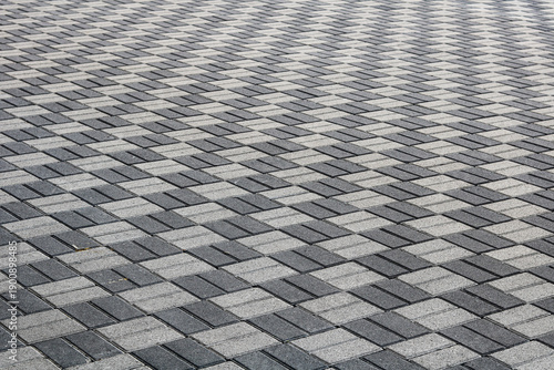 Interlocking light and dark grey paving stones forming a repeating geometric pattern, creating a clean and orderly outdoor surface.