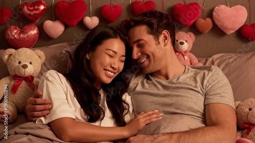 A romantic couple lies in bed surrounded by heart balloons and teddy bears on Valentine's Day in a cozy video